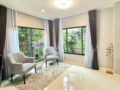 Elegant living room with large windows and garden view, featuring modern armchairs and stylish decor.