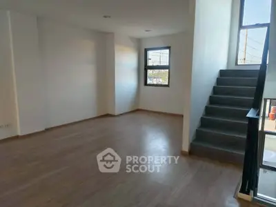 Spacious modern living room with wooden flooring and large windows, featuring a staircase leading to upper level.
