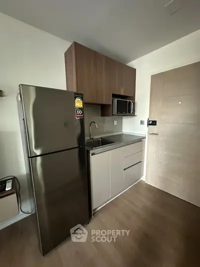 Modern compact kitchen with stainless steel fridge and microwave in sleek apartment.
