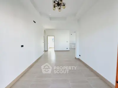 Spacious empty room with elegant chandelier and bright natural light.