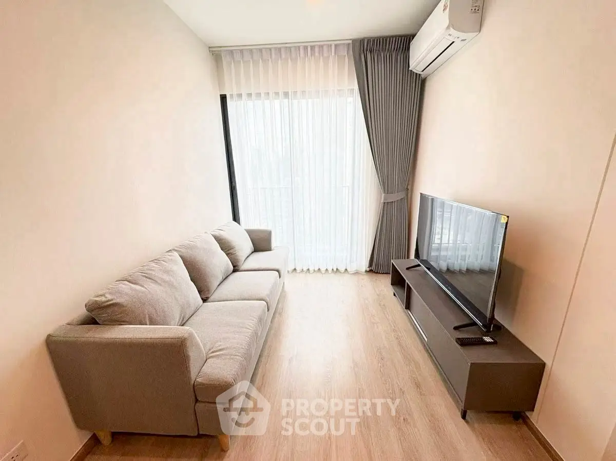 Modern living room with cozy sofa and flat-screen TV, featuring elegant curtains and wooden flooring.
