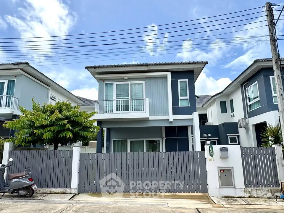 Modern two-story house with balcony and gated front yard in a suburban neighborhood.
