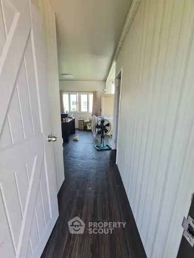 Spacious hallway leading to a bright living area with modern decor and wooden flooring.