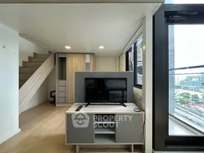 Modern living room with TV, staircase, and large windows offering city views.