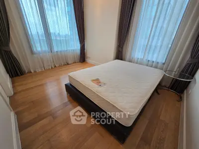 Spacious bedroom with large windows and hardwood floors in modern apartment.