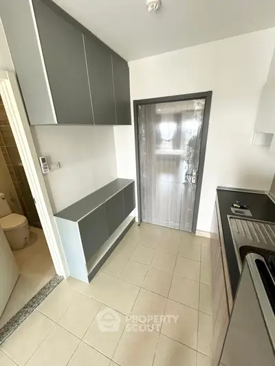 Modern kitchen with sleek cabinets and tiled floor, adjacent to a compact bathroom.