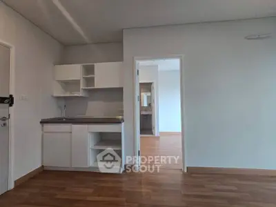 Modern apartment interior with compact kitchen and wooden flooring, showcasing minimalist design and open space.