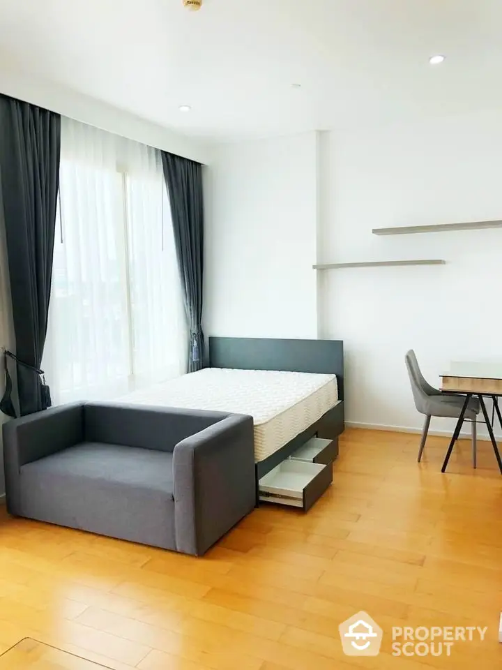 Modern bedroom with sleek furniture and natural light, featuring a cozy bed and stylish sofa.