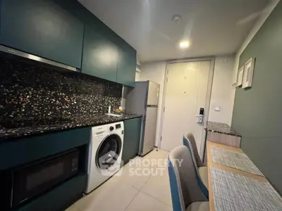 Modern kitchen with sleek cabinetry, washing machine, and dining area in compact apartment.