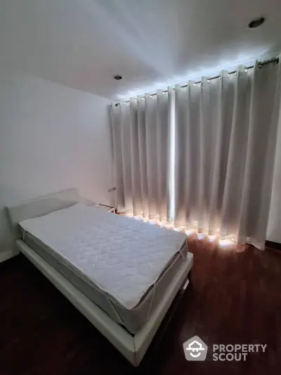 Cozy bedroom with polished hardwood floors and elegant white drapery, enhanced by ambient lighting for a serene living space.