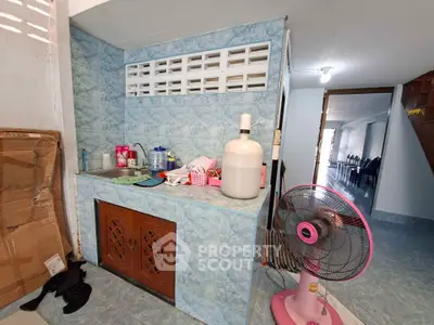 Compact kitchen area with blue tile walls and a pink fan, showcasing practical design.
