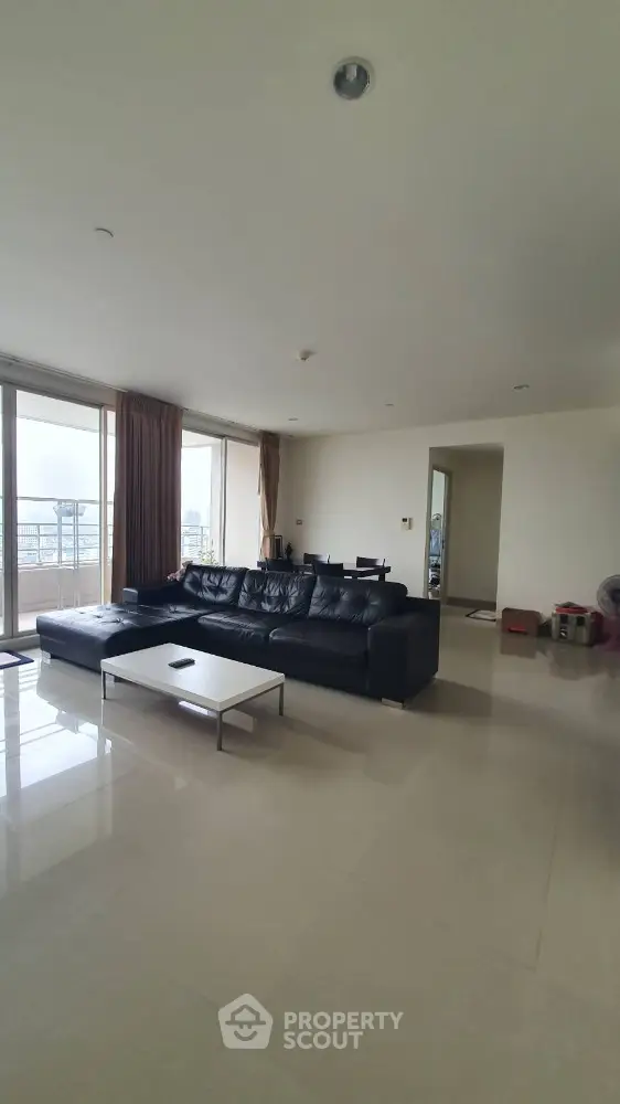 Spacious living room with modern black leather sofa and large windows offering natural light.