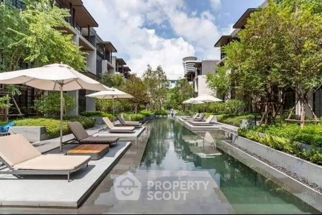 Luxurious outdoor pool area with sun loungers and lush greenery in a modern residential complex.