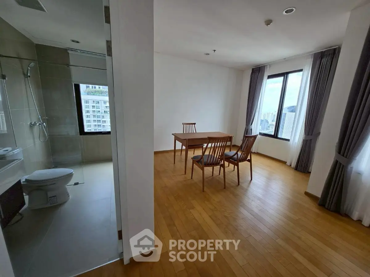 Spacious apartment with wooden flooring and large windows offering city views, featuring a minimalist dining area.