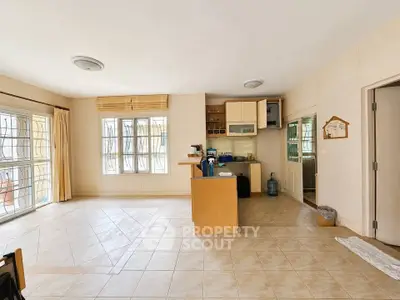 Spacious open-plan living room with kitchen, featuring large windows and tiled flooring.