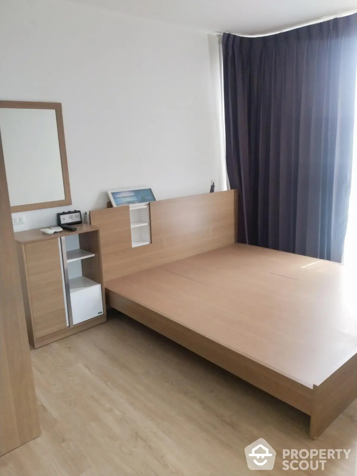 Modern minimalist bedroom with wooden bed and floor, large window with dark curtains.