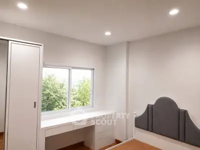Modern bedroom with built-in wardrobe and desk, featuring a large window with a lush green view.