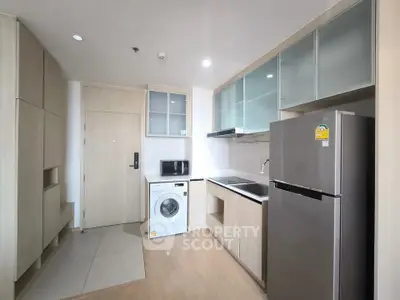 Modern kitchen with washing machine and stainless steel fridge in compact apartment.