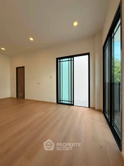 Spacious modern room with wooden flooring and large windows offering natural light.