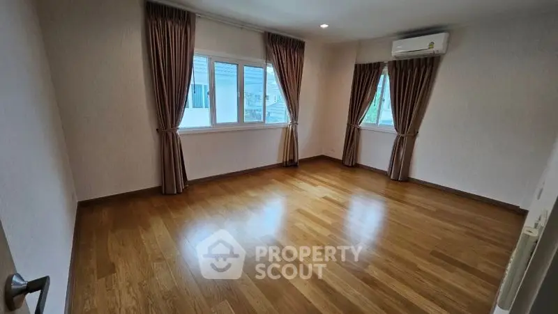 Spacious empty room with wooden flooring and large windows, perfect for customization.