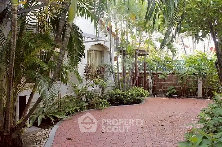 Charming garden patio with lush greenery and paved walkway in serene residential setting.