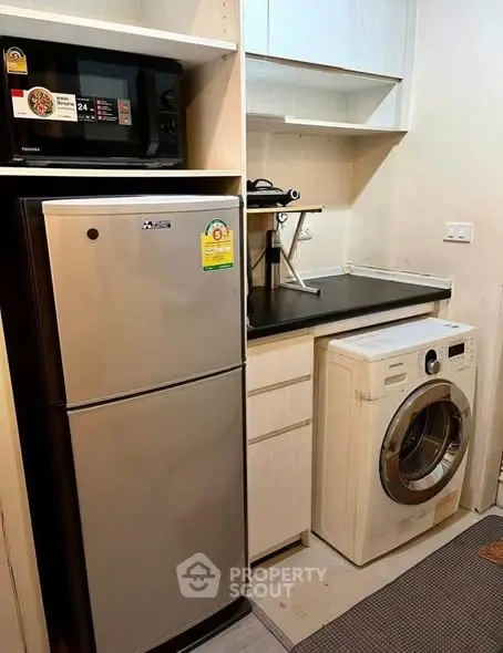 Compact kitchen with fridge, microwave, and washing machine in modern apartment.