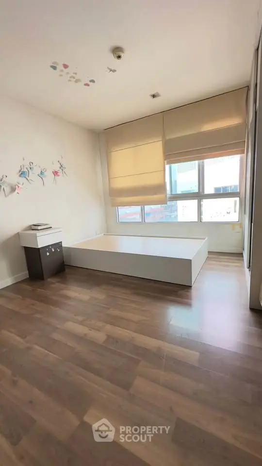 Spacious bedroom with wooden flooring and large windows for natural light.