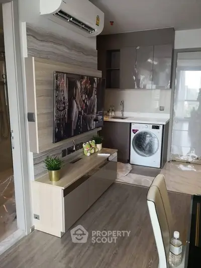 Modern living room with sleek TV setup and compact kitchen area featuring a washing machine.