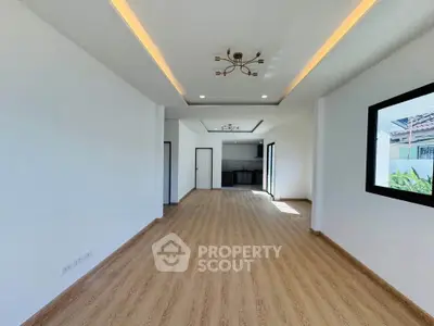 Spacious modern living room with wooden flooring and recessed lighting, open layout leading to a sleek kitchen.
