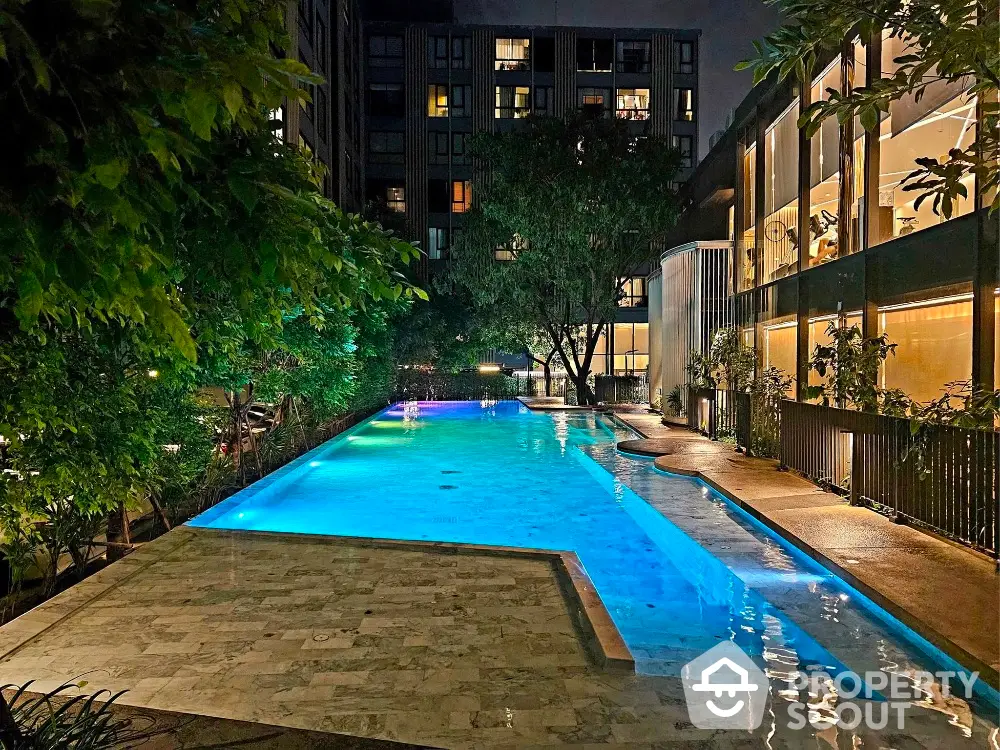 Luxurious residential pool area with ambient lighting and lush greenery at night.