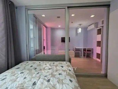 Modern bedroom with sliding glass doors leading to a stylish living area, featuring contemporary decor and ample natural light.