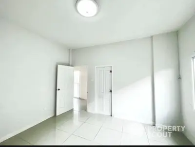 Bright empty room with white walls and tiled floor, featuring a door leading to another space.