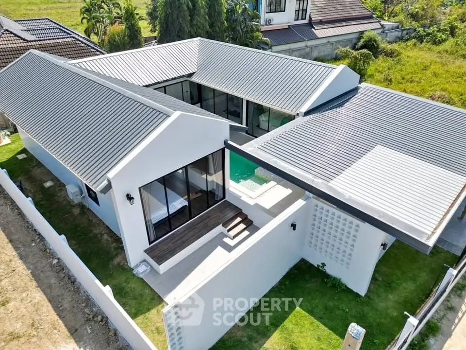 Modern white villa with sleek metal roof and private pool, surrounded by lush greenery.