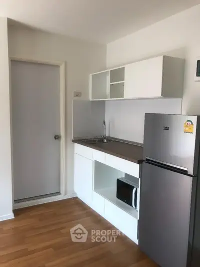 Modern compact kitchen with sleek cabinetry and stainless steel fridge in a cozy apartment.