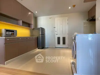 Modern kitchen with sleek cabinets, fridge, and washing machine in a spacious layout.