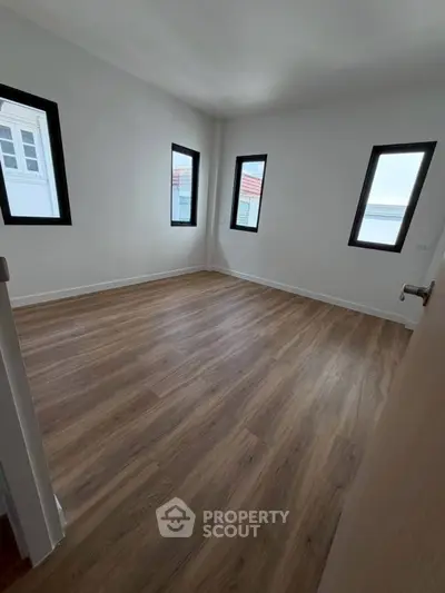 Spacious empty room with wooden flooring and multiple windows, ideal for customization.