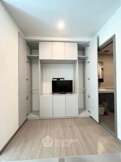 Modern living room with built-in storage and TV, adjacent to a bathroom, showcasing sleek design and functionality.