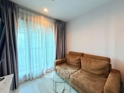 Cozy living room with plush brown sofa and glass coffee table, featuring large window with elegant curtains.