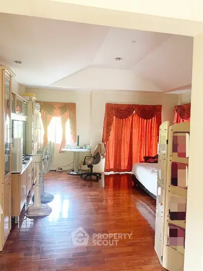 Spacious multi-purpose room with polished wooden floors, vibrant red curtains, and ample natural light, perfect for living and sleeping areas.
