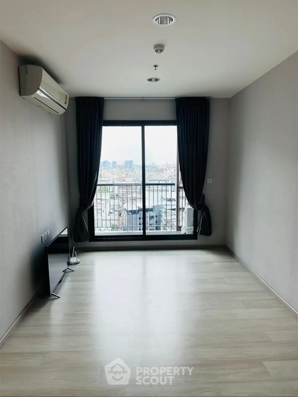 Spacious living room with large window and city view, featuring modern air conditioning and sleek flooring.