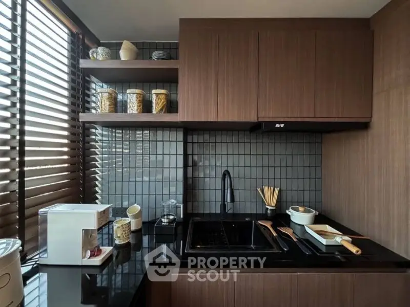 Modern kitchen with sleek cabinets and black countertop, featuring coffee machine and stylish backsplash.