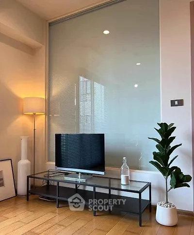 Modern living room with sleek TV stand, stylish lamp, and potted plant on wooden floor.