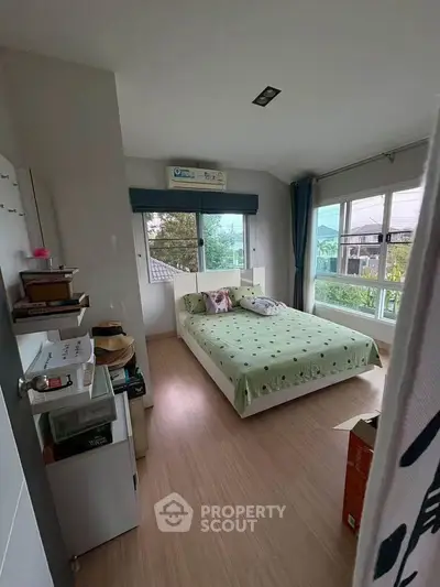 Cozy bedroom with large windows and green bedspread, offering a bright and inviting atmosphere.