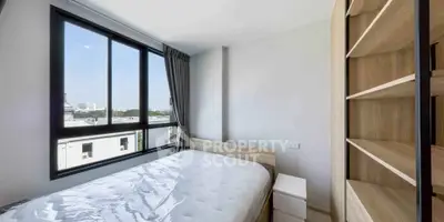 Bright bedroom with large window and built-in shelving, offering a cozy and modern living space.