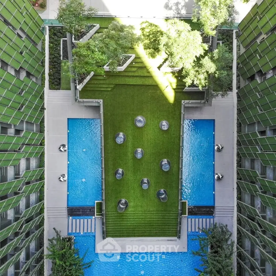 Stunning aerial view of modern building courtyard with lush greenery and blue pools, perfect for urban living.