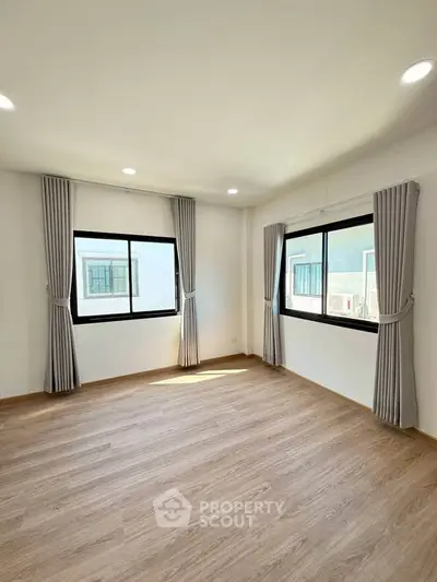 Spacious sunlit room with large windows and elegant curtains, perfect for a cozy living space.