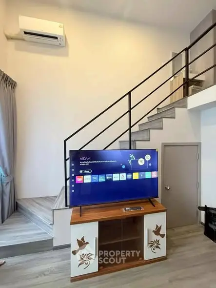 Modern living room with stylish staircase and mounted TV, showcasing open layout and sleek design.