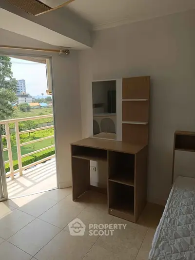 Bright bedroom with balcony access and modern wooden desk overlooking lush greenery.