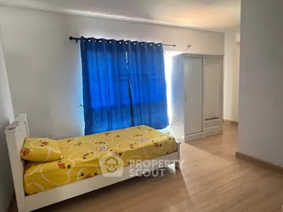 Bright bedroom with single bed and wardrobe, featuring blue curtains and wooden flooring.