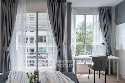 Bright bedroom with large windows and study area, featuring elegant gray curtains and modern decor.